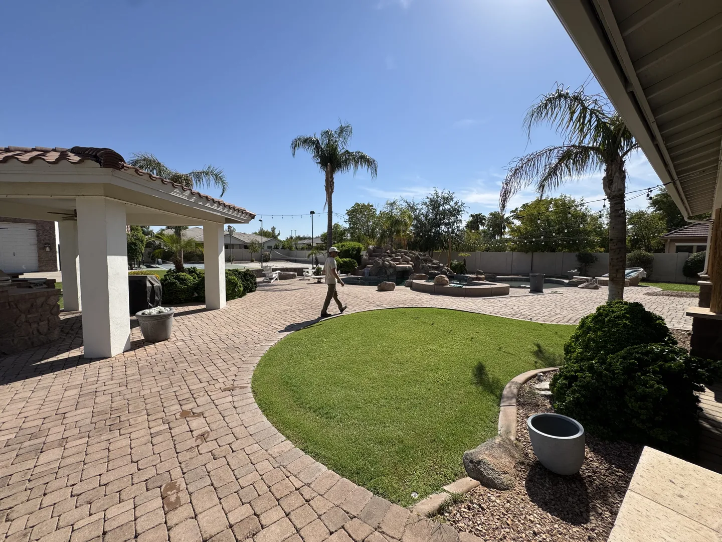 Wide stone paved terrace with lawn, palms, and a shaded pavilion