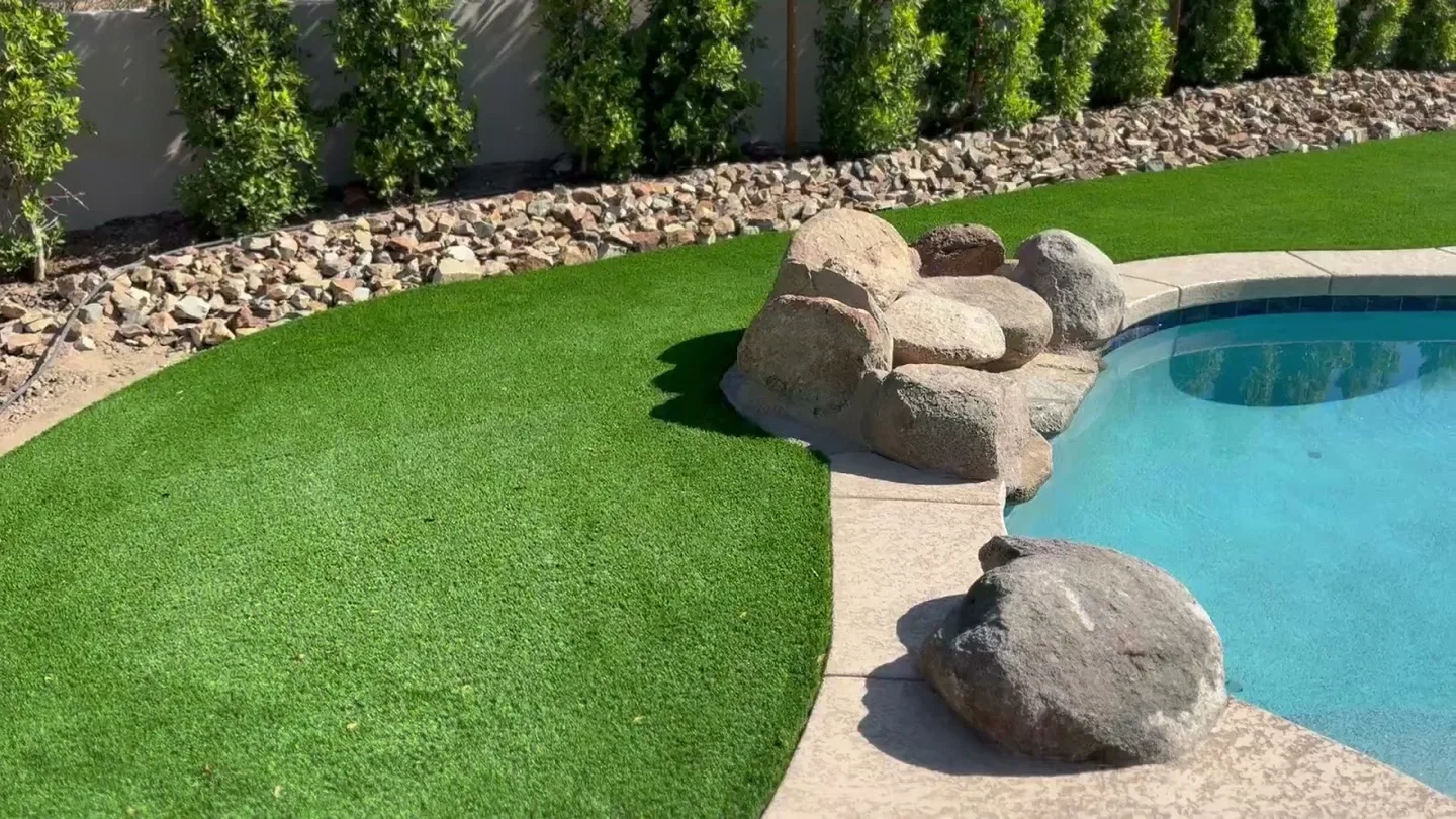 Bright green turf and river rock curving around a backyard pool