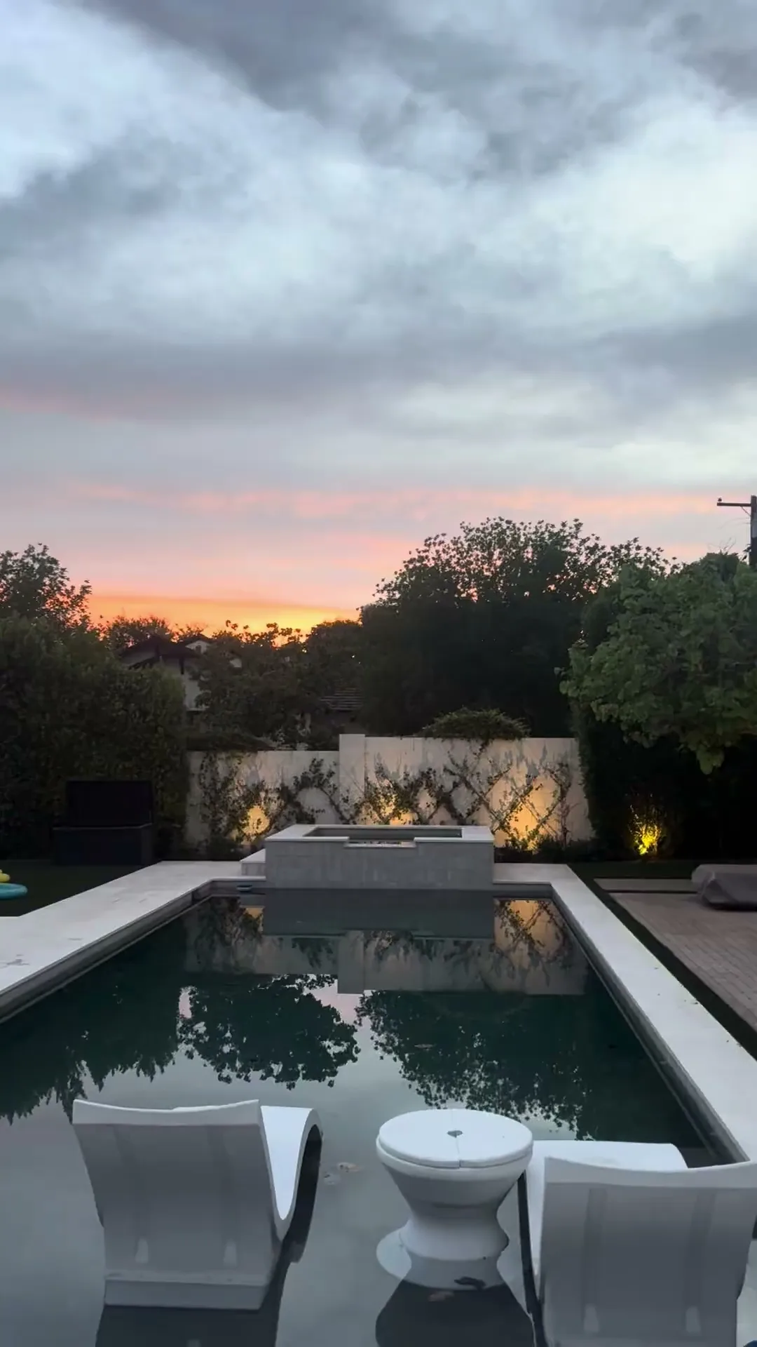 Pool and outdoor seating framed by landscape lighting under a sunset sky